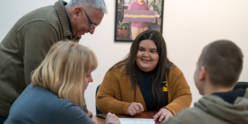 A woman in an IRC shirt sits accross from three individuals, helping them with paperwork
