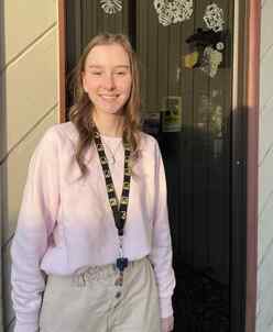 A young woman stands smiling next to a glass door wearing a lanyard with the IRC logo. 