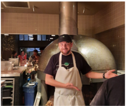 Client standing in front of brick oven