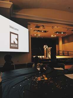 young man speaking on stage with an IRC sign next to the stage. 