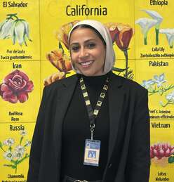Mawada smiles in front of painted mural of flowers with IRC lanyard