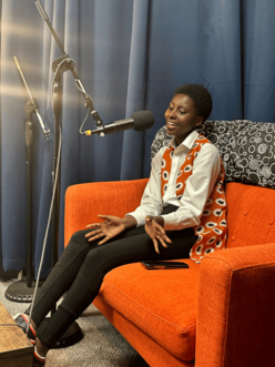 Woman sitting on orange couch talking into microphone.