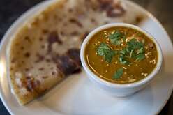 White plate featuring a bowl of beans garnished with parsley alongside a piece of flatbread. 