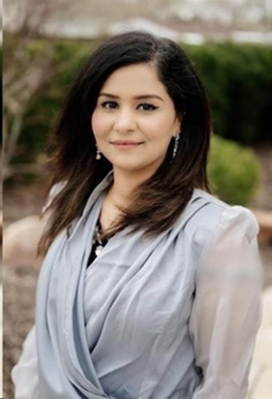 Portrait of Khatima in a gray blouse, dark hair on a blurred natural background.