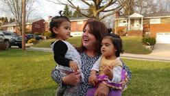 Joanne holding to toddlers in her arms and smiling outside of a neighborhood.