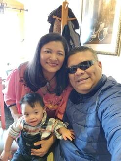 Young family with their kid posing for a selfie with a coat rack in the background.