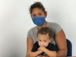 A woman wearing a mask sits with her child on her lap at an IRC-run clinic at the Simón Bolívar bridge.