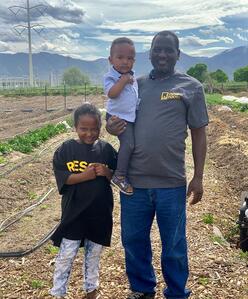 Family standing amidst farm land with mountains in the background.