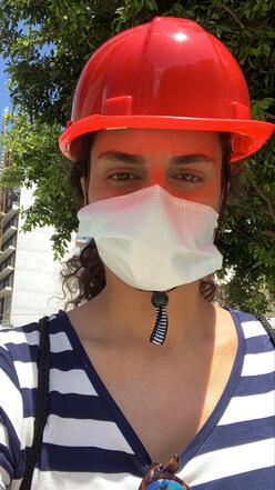 A selfie photo taken by Rebecca Mouawad. She is wearing a red hard hat and a white surgical mask.