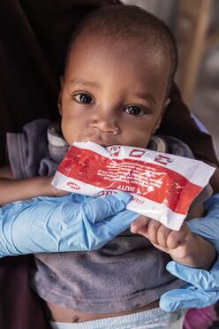 Amina’s son, while sitting on her lap, eats Plumpy’Nut.