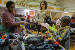 A mother and two children select winter accessories from a pile of gloves at the IRC's Warm Welcome Winter Clothing Drive, as the volunteer assisting them stands in the background.