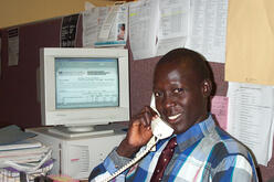 A former Sudanese "Lost Boy" who was resettled in the United States is at work next to a computer, answering a telephone.