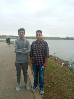 Ehsanullah and his son stand in front of a body of water