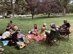Nine women participating in the IRC in Salt Lake City's Women's Health & Healing Group sit in a circle on blankets and chairs on a grass lawn