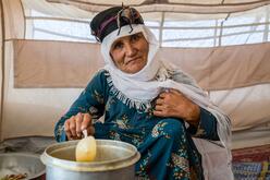 A 67-year-old Afghan woman stirs a pot as she sits cooking in a tent in the camp where her family lives after being displaced by drought.
