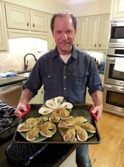 Paul Parisi, standing in a kitchen and holding a pan of Oysters Rockefeller fresh out of the oven.