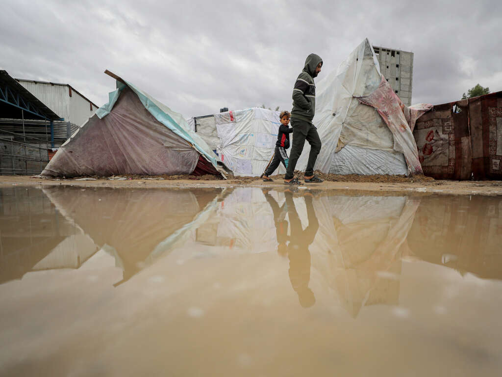 한 소년이 아버지와 함께 물에 잠긴 임시 텐트 사이를 걸어가고 있습니다.