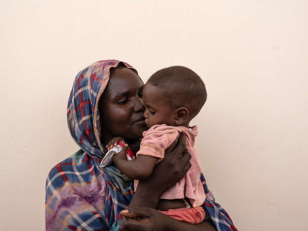 A Sudanese mother holds a young child close in her arms.