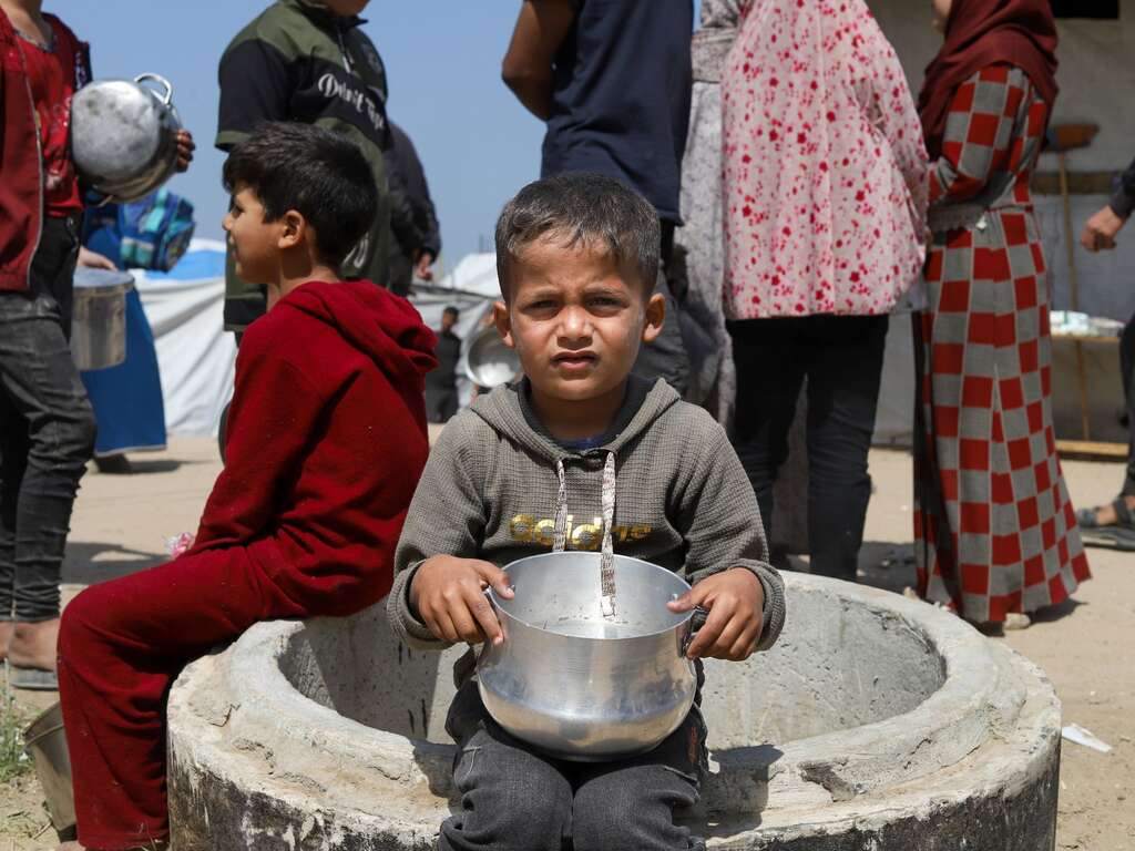 A Gazan child sits with an empty bowl waiting for aid
