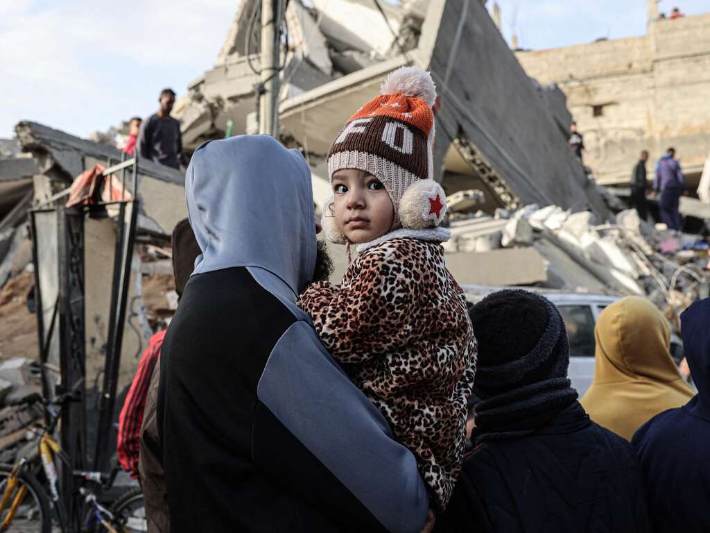 A young Palestinian child and their mother examine a destroyed building in their neighborhood
