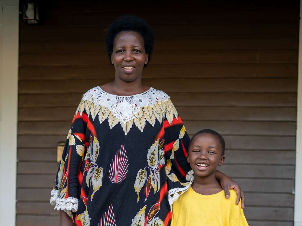 A mother and a son pose for a photo in front of their home.