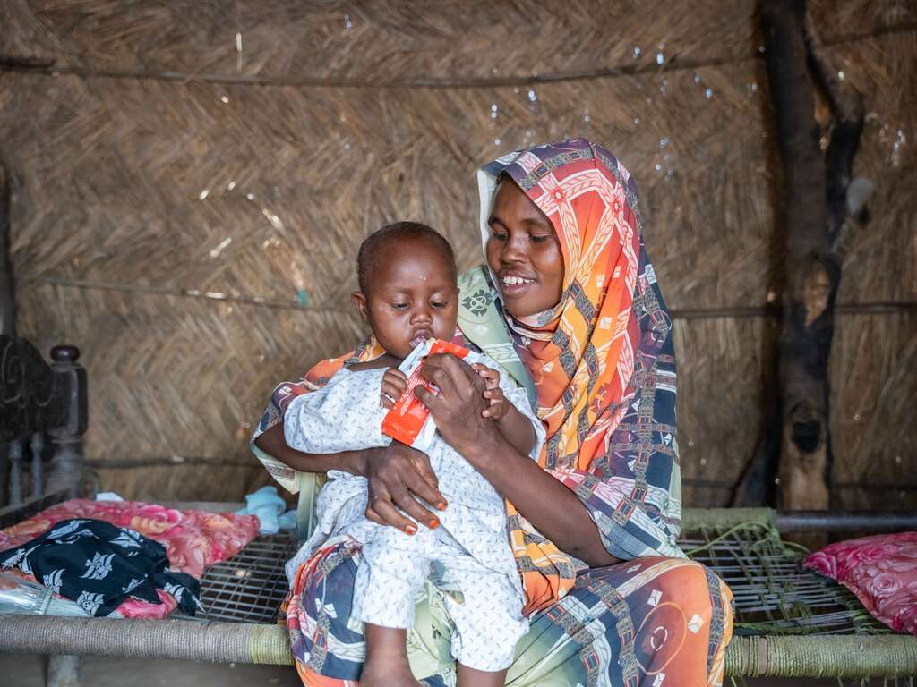 A Sudanese mother feeds her young child a malnutrition treatment packet, provided by the IRC