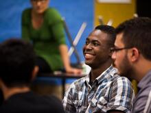 Zwei junge Männer schauen links aus dem Bild und lachen.