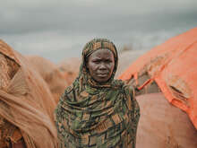 Portrait of a woman standing in front of a series of huts in the Somali desert.