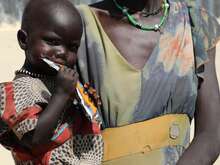 A child in her mother’s arms eats a packet of high-protein peanut paste to combat malnutrition in South Sudan.