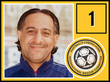 Ein Mann mittleren Alters mit welligem, dunklem Haar und einem warmen Lächeln trägt eine dunkelblaue Jacke und schaut in die Kamera.