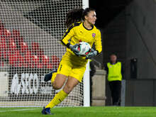 Eine Torhüterin in gelbem Trikot hält den Fußball während eines Spiels.