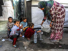 En kvinna i Gaza fyller vatten i flaskor. Barn sitter på gatan.
