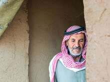 Ein älterer Mann in traditioneller Kleidung steht im Eingang eines einfachen Lehmhauses in Syrien.