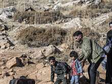 A family walks through an arid landscape with their belongings.