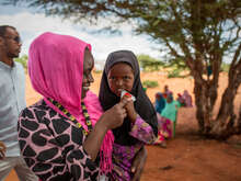 한 어린이가 엄마 품에 안겨 영양실조 치료식을 먹고 있습니다.