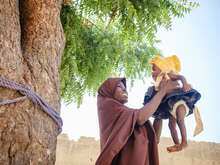 한 엄마가 아기를 하늘로 안아 올리며 밝게 웃고 있습니다.