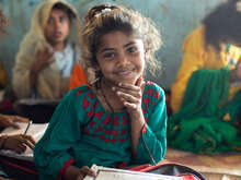 En 7-årig flicka sitter på golvet med en lärobok framför sig.