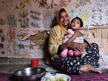 한 엄마가 바닥에 앉아서 아기를 안고 웃고 있습니다.