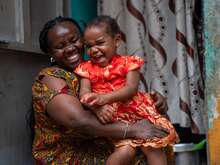 한 우간다 엄마가 아기를 품에 안고 함께 활짝 웃고 있습니다.