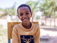 한 소년이 카메라를 바라보고 밝게 웃고 있습니다.,