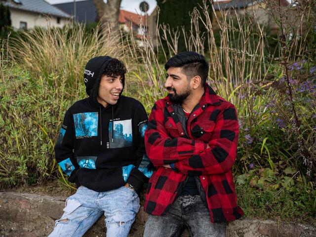 Ali und Mehdi sitzen draußen und reden miteinander.