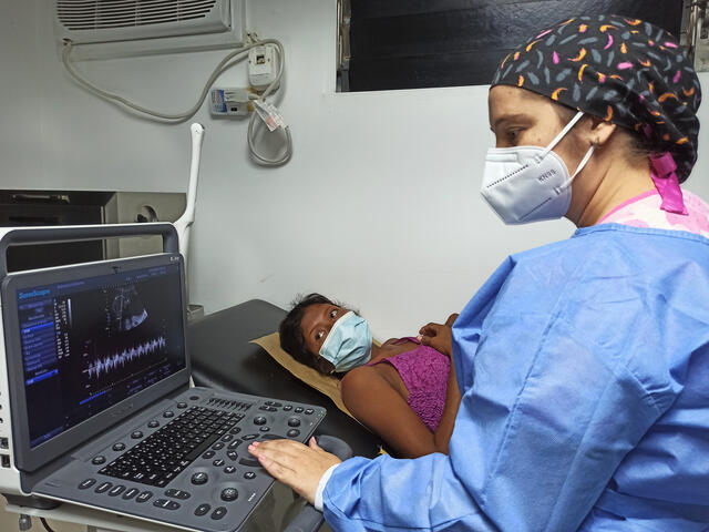Daisy, a Venezualan woman, looks at the screen as a tech reviews her sonogram at a prenatal checkup