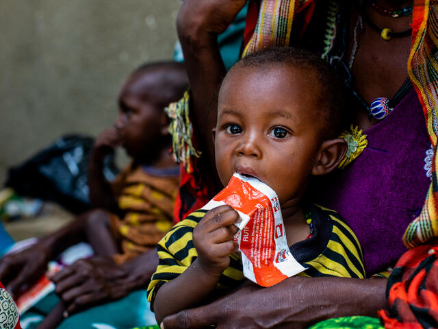 A child in Chad sits in his mother's lap and eats a RUTF bar - an effective treatment for acute malnutrition.