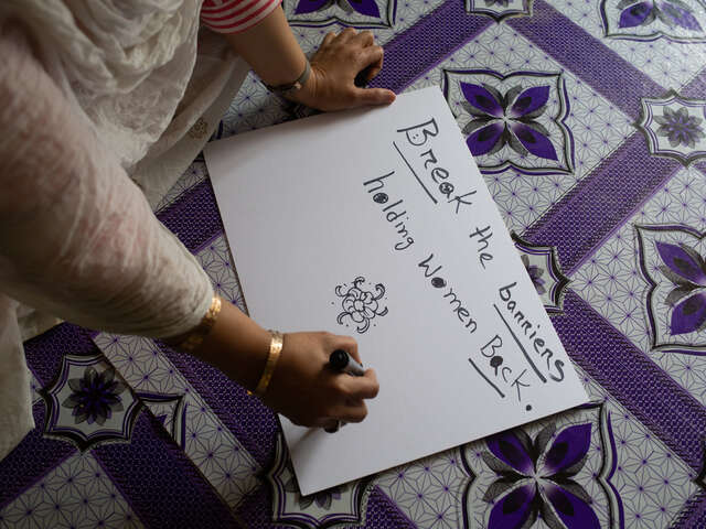 Kvinna skriver slagord för jämställdhet på ett plakat.