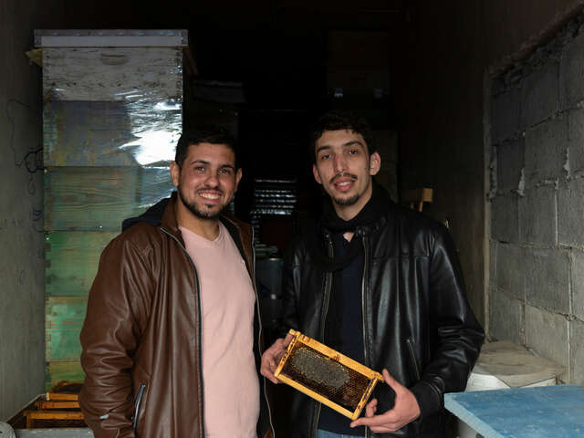 Huthaifa, 32, left, and Ahmad, 28, pose with a small hive frame at their store.
