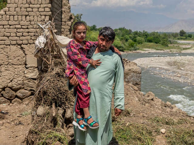 Pappa och dotter i Afghanistan står vid familjens hem som förstörts översvämningar.