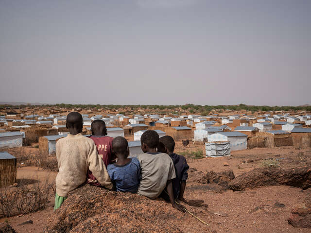 Barn sitter på en kulle och tittar ut mot ett flyktingläger i Tchad
