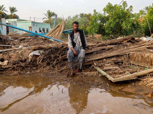 En man i Sudan sitter vid en förstörd byggnad i ett översvämmat område