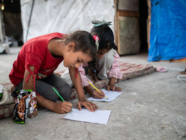 Två barn i Gaza sitter utanför ett tält och ritar.