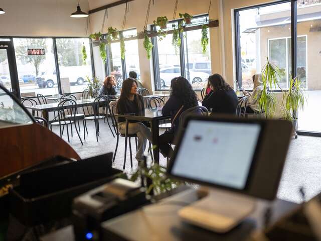 Interior of Spice on 9th Cafe behind the counter, tablet point of sale system in the foreground with customers seated at tables in the background.